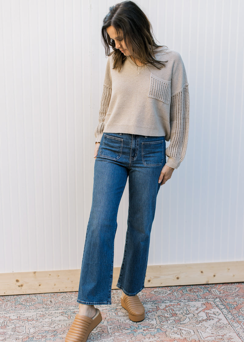 Model wearing jeans, clogs and an oatmeal sweater with crochet long sleeves and a crochet pocket.