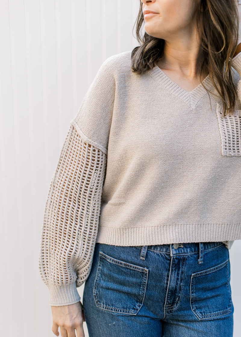 Model wearing a slightly cropped oatmeal v-neck sweater with crochet long sleeves.