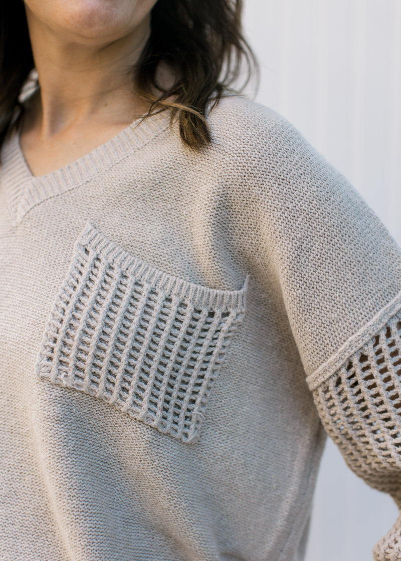 Close up of crochet pocket and long sleeve on an oatmeal sweater with a v-neck.