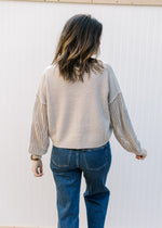 Back view of Model wearing an oatmeal v-neck sweater with crochet long sleeves and a crochet pocket.