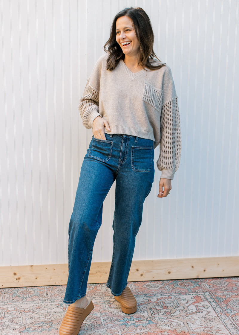 Model wearing jeans with a slightly cropped oatmeal sweater with crochet long sleeves.