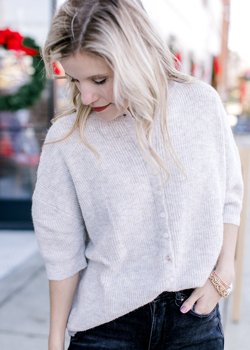 Model wearing an mottled oatmeal yarn sweater with mother of pearl buttons and an oversized fit.