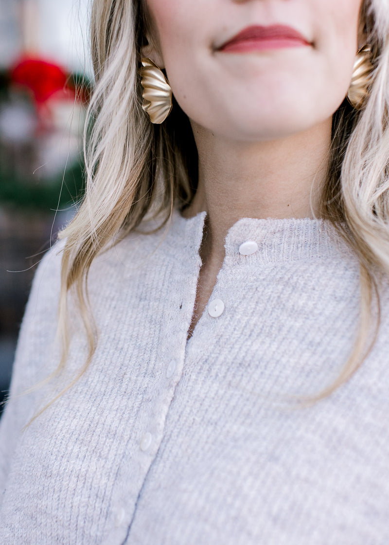 Close up of mother of pearl buttons on a ribbed short sleeve sweater with an oatmeal color. 