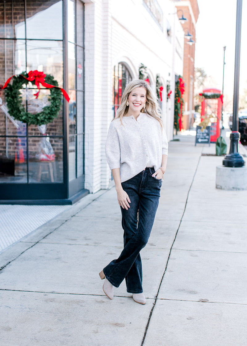 Model wearing jeans and an oatmeal sweater with mother of pearl buttons and an oversized fit.