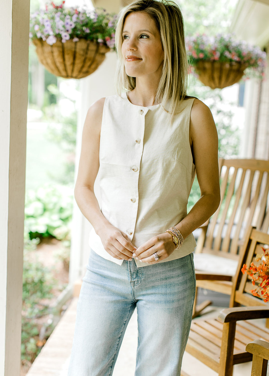Model wearing a cream sleeveless vest-style top with working button front and adjustable tie back.