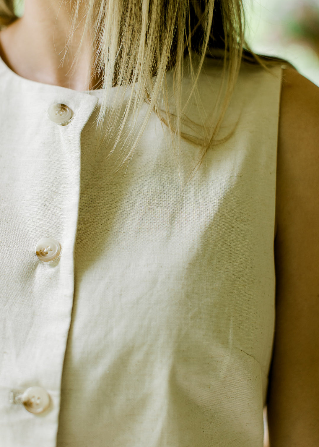 Close up of button closure and sleeveless fit on an oatmeal colored linen top with tie back. 