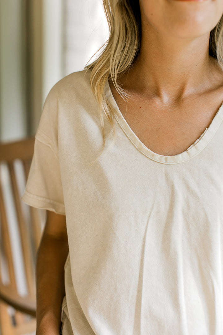 Close up of raw hemlines, v-neck and short sleeves on an oatmeal loose fit tee. 