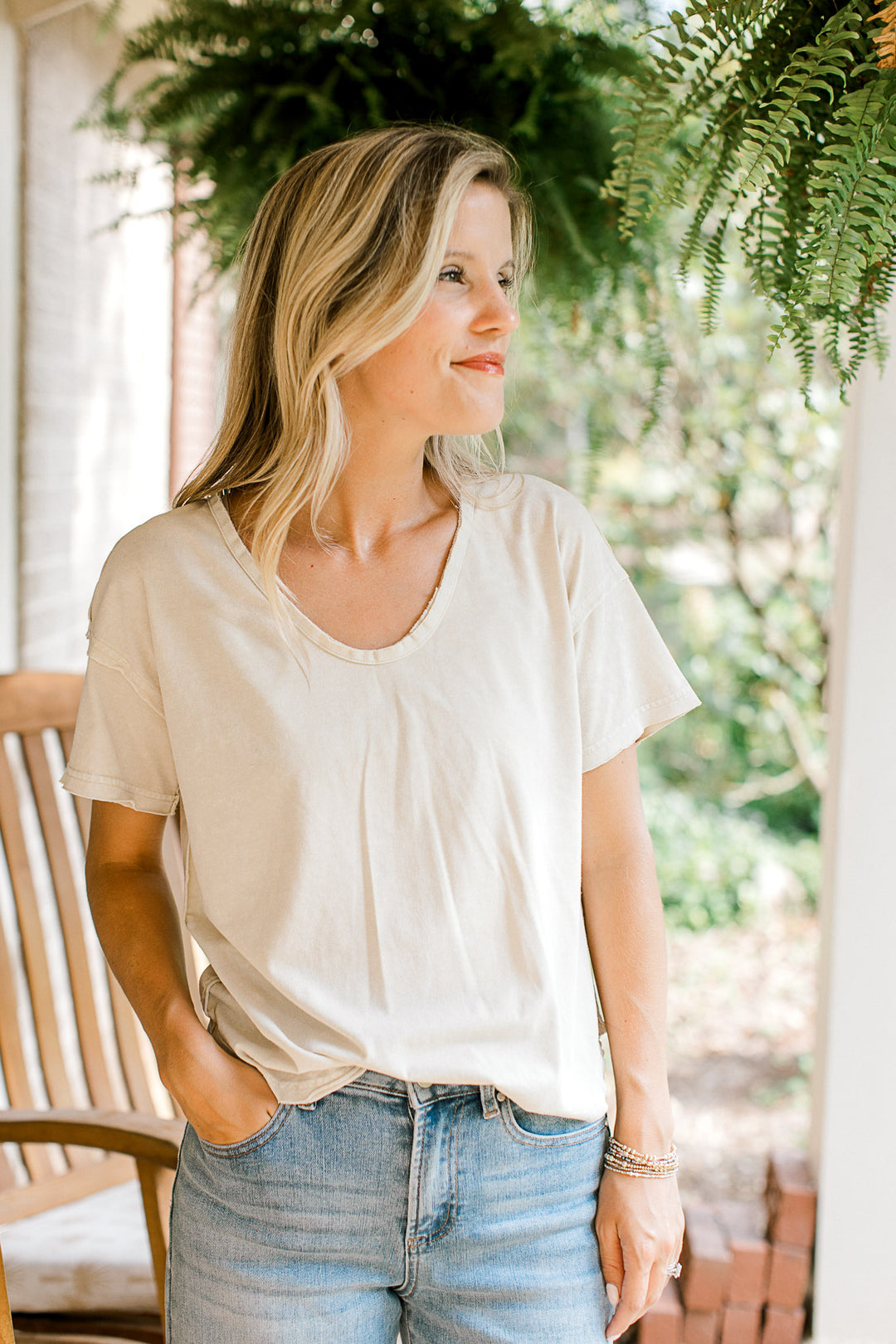 Model wearing a v-neck oatmeal top with raw edges, short sleeves and a loose fit. 
