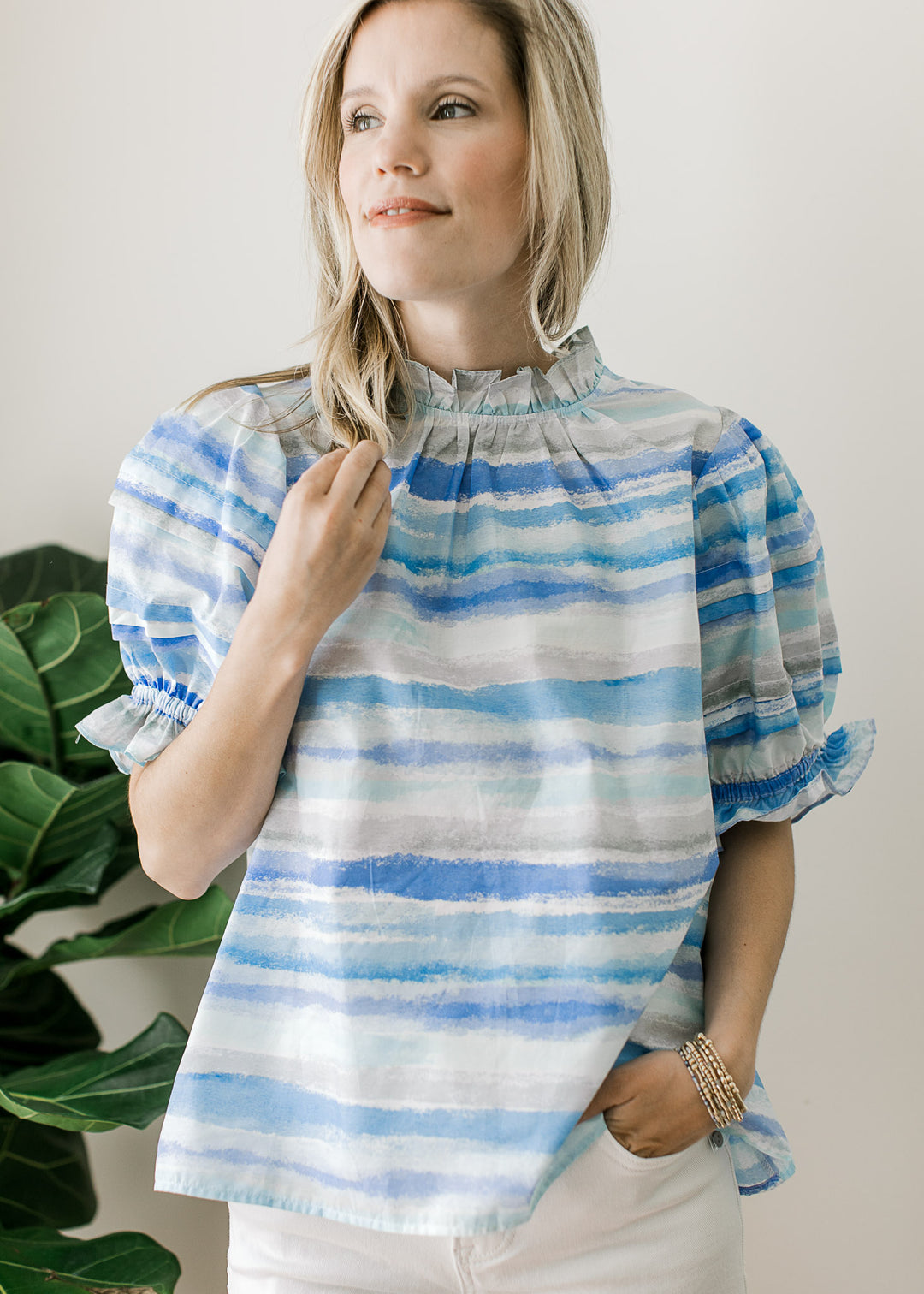 Model wearing a top of varied shades and lines of blue, ruffle detail at neck and bubble sleeves.