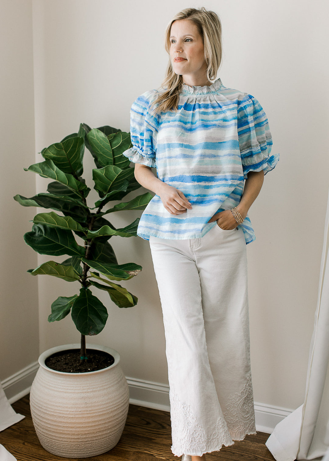Model wearing a top with lined varied shades of blue, ruffle detail at neck and bubble sleeves.