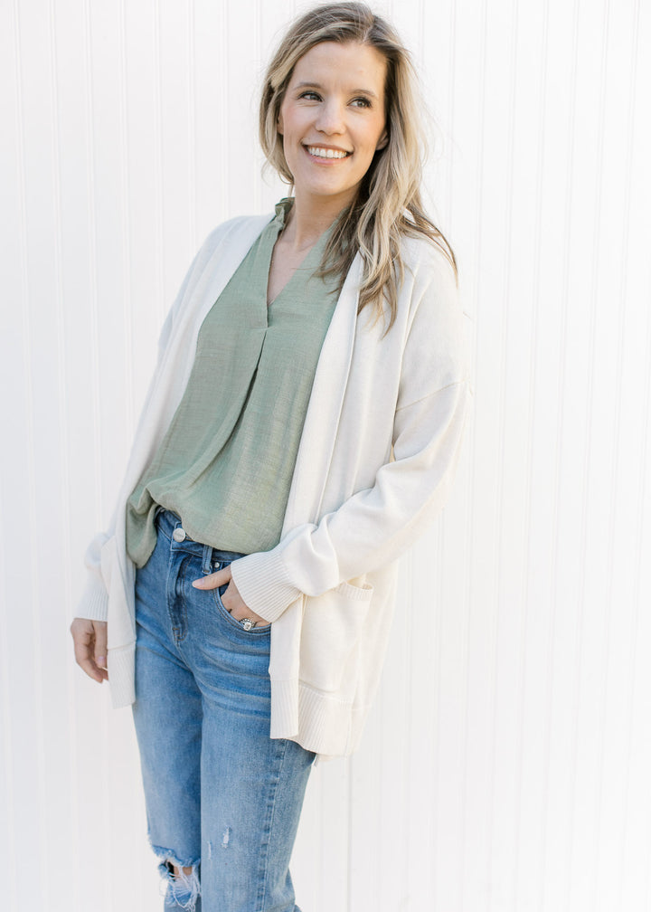 Model wearing an off white cardigan with an open front, long sleeves and patch pockets.