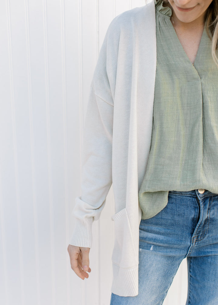 Close up of Model wearing an off white cardigan with an open front, long sleeves and patch pockets.
