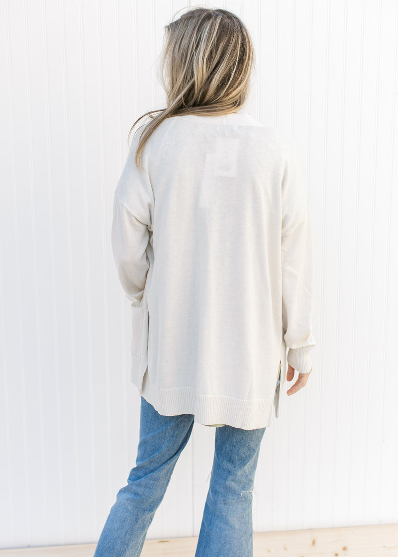 Back view of Model wearing an off white cardigan with an open front, long sleeves and patch pockets.