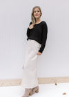 Model wearing a black top and booties and a cream denim skirt with a front slit and a midi length.