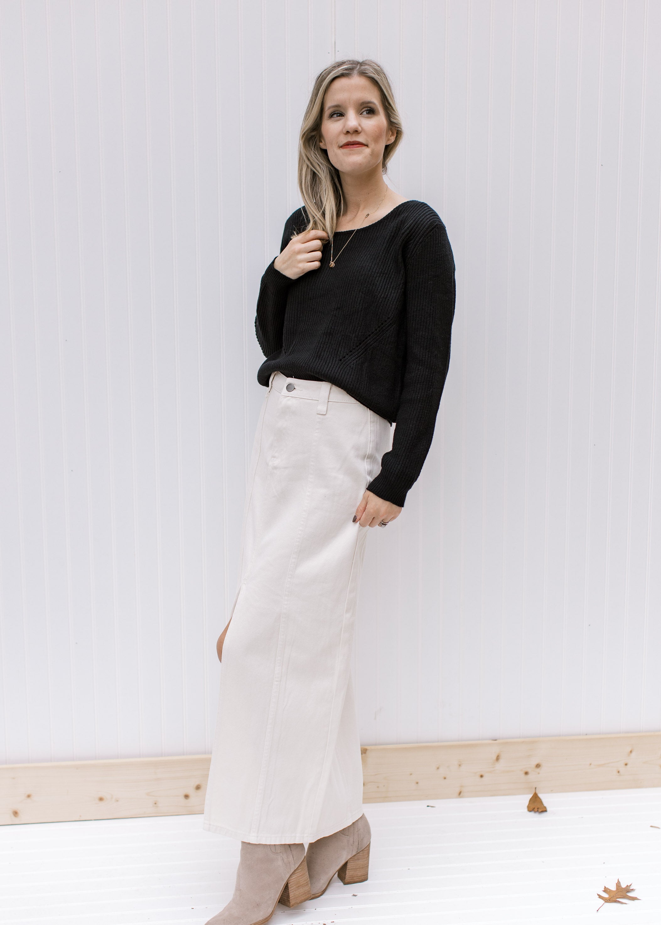 Model wearing a black top and booties and a cream denim skirt with a front slit and a midi length.