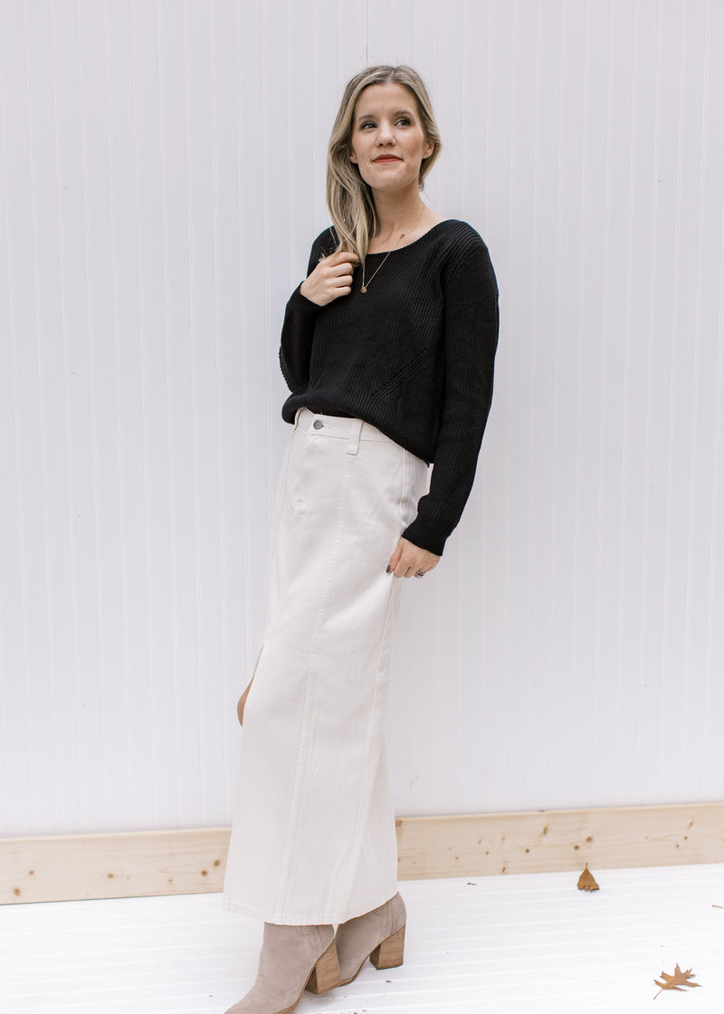 Model wearing a black top and booties and a cream denim skirt with a front slit and a midi length.