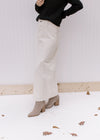 Side view of a model wearing a black top and booties with a cream denim skirt with a front slit