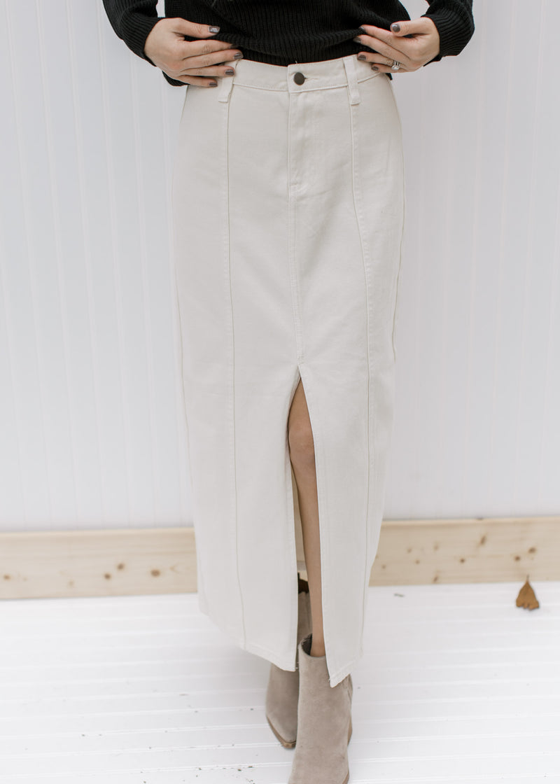 Close up view of the front slit on a cream colored denim skirt with a midi length. 