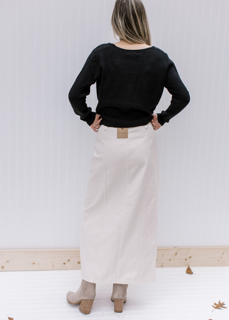 Back view of model wearing a black top and a cream denim skirt with a front slit and a midi length.