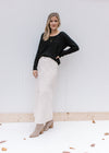 Model wearing a cream denim skirt with a midi length and a front slit with a black top. 