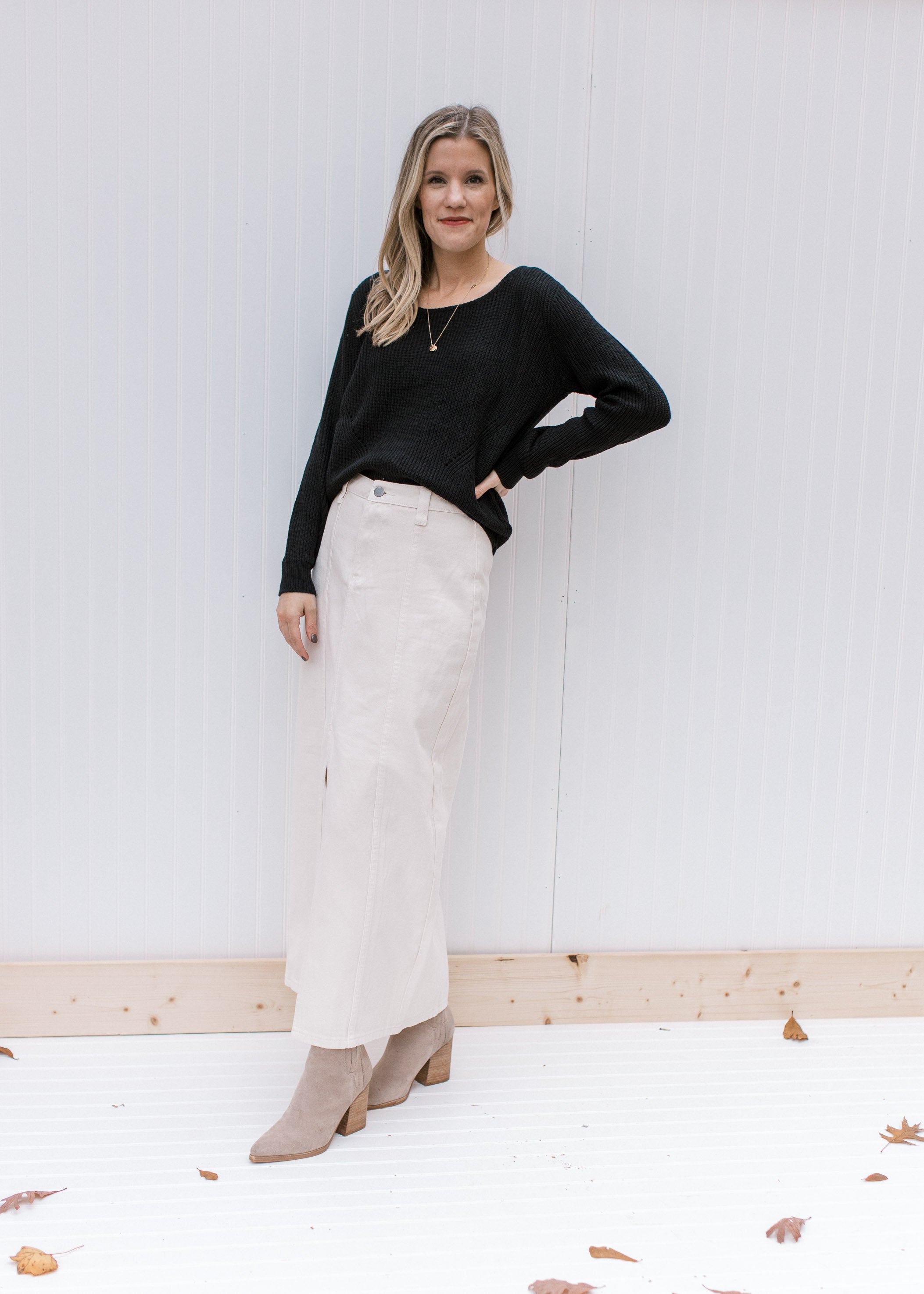 Model wearing a cream denim skirt with a midi length and a front slit with a black top. 