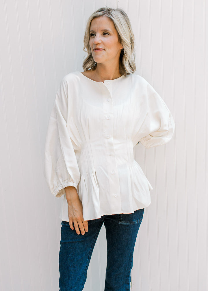 Model wearing jeans and an off-white top with button-front, elbow-length sleeves and pleated waist.