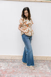 Model wearing jeans and a cream top with pink floral pattern and flutter short sleeves.