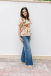 Model wearing jeans, sandals and a cream top with pink floral pattern and short sleeves.