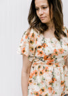 Close up of flutter sleeves and square neck on a cream top with pink floral pattern. 
