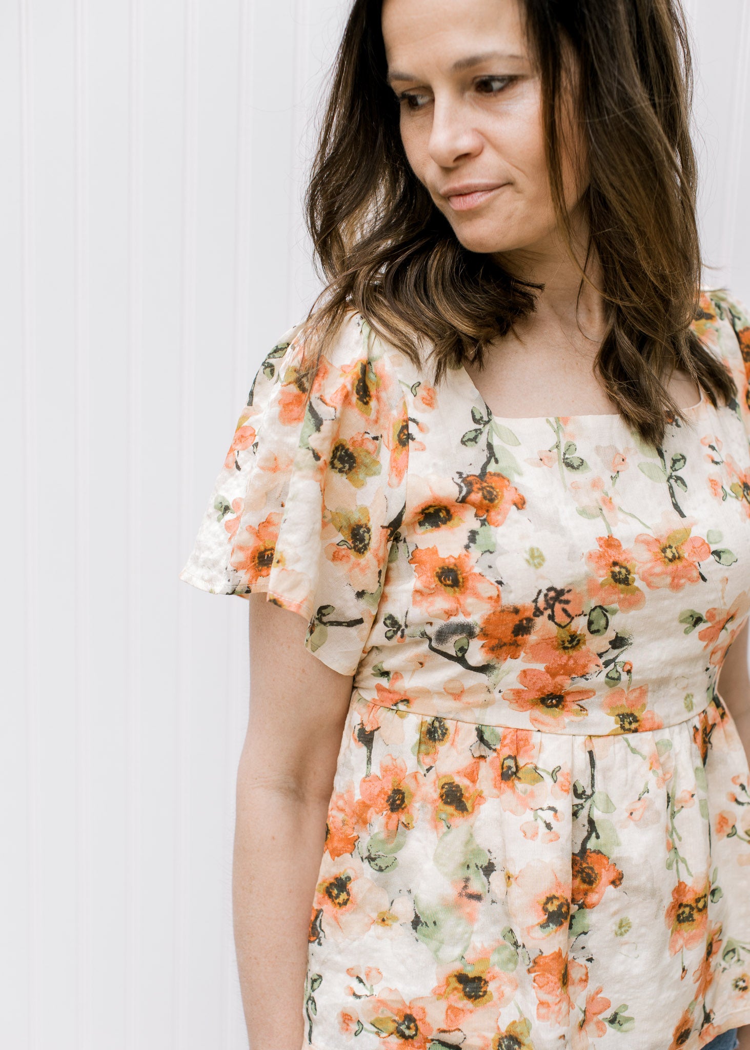 Close up of flutter sleeves and square neck on a cream top with pink floral pattern. 