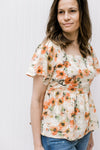 Model wearing a cream top with pink floral pattern, square neck and flutter short sleeves. 