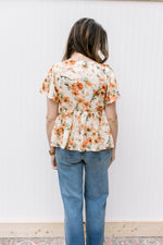 Back view of Model wearing a cream top with pink floral pattern and flutter short sleeves.