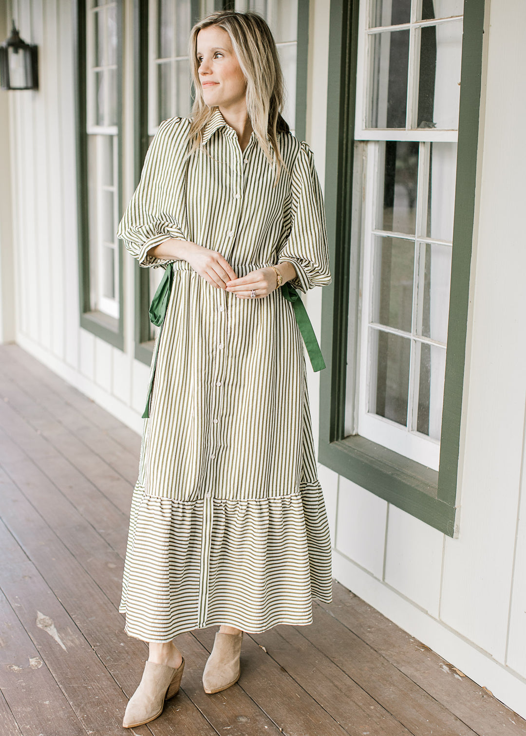 Model wearing a cream midi with olive stripes, buttons, elastic waist with side ties and 3/4 sleeve.
