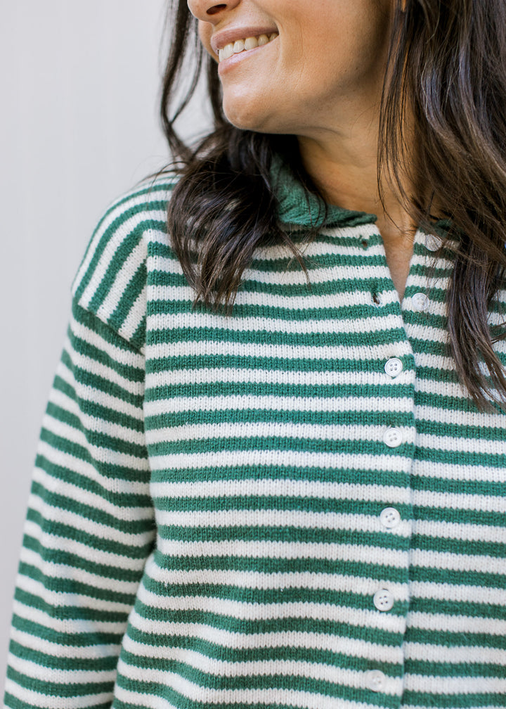 Close up of buttons front on a long sleeve olive and ivory striped sweater with green trim and neck.