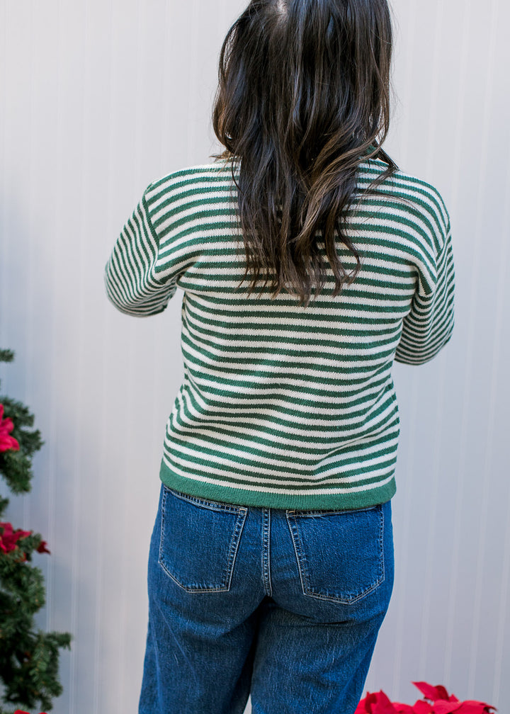 Back view of Model wearing an olive and ivory striped sweater with green trim and long sleeves. 