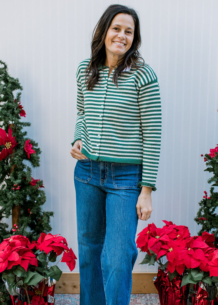 Model wearing jeans and an olive and ivory striped button up with green trim and long sleeves. 