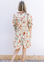 Back view of Model wearing a cream dress with olive and rust floral and 3/4 poet sleeve.