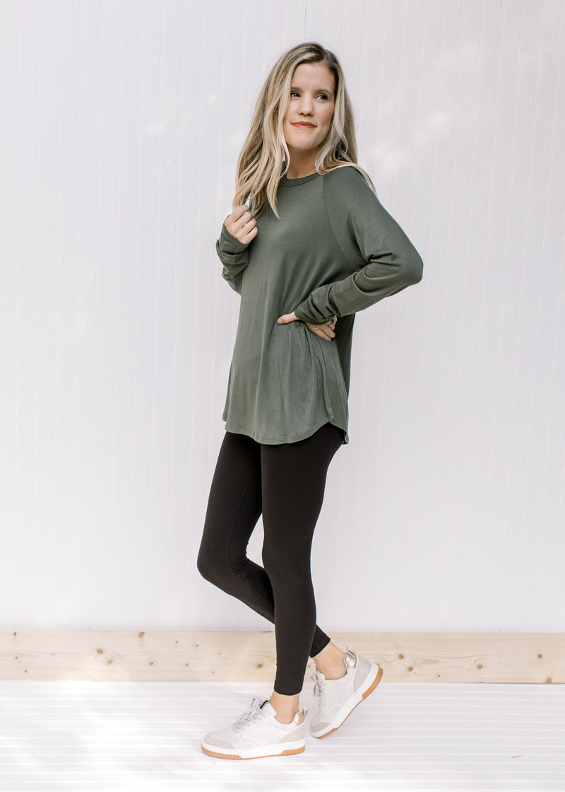 Model wearing black leggings with sneakers and an olive top with a round neck and long sleeves. 