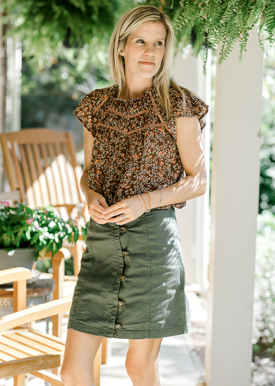 Model wearing an olive colored, above the knee, button up skirt with a brown blouse. 