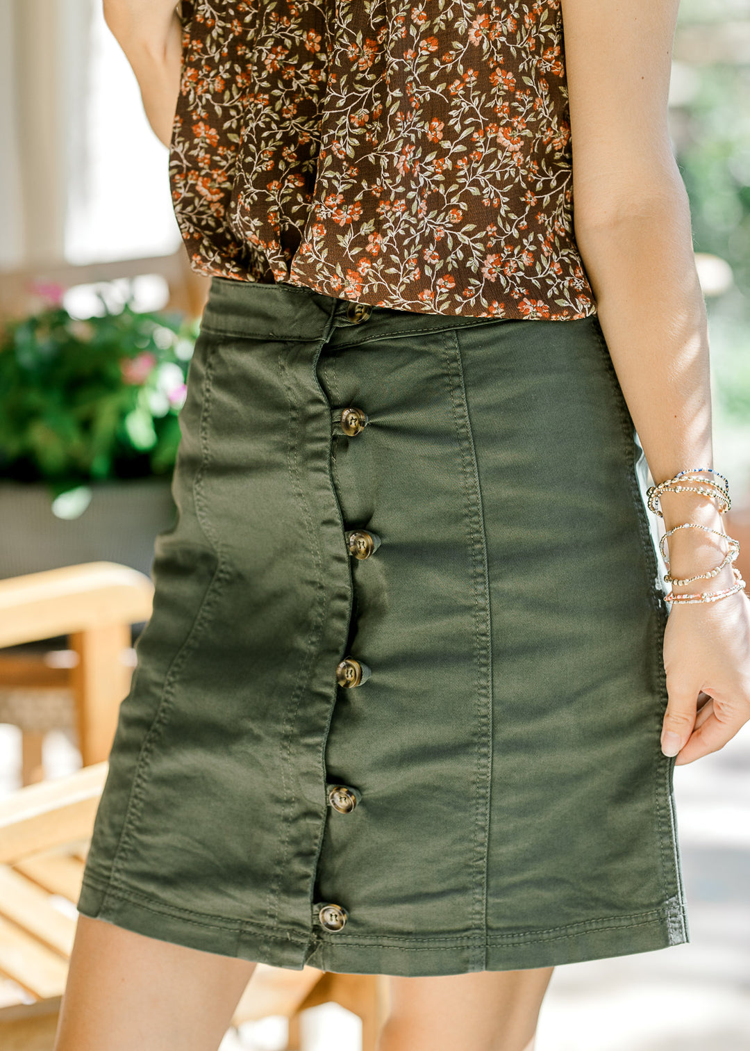 Close up of olive above the knee skirt with brown button front and seams for added texture. 