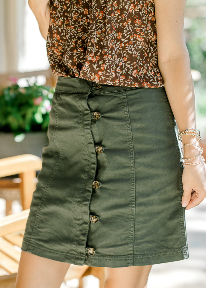 Close up of olive above the knee skirt with brown button front and seams for added texture. 