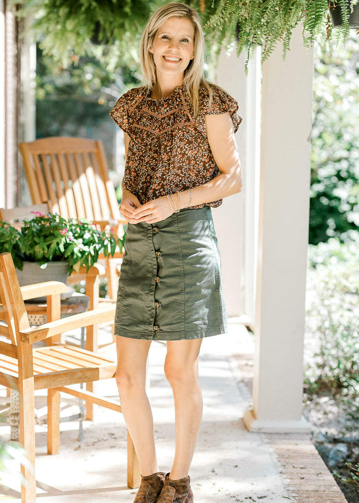 Model wearing an olive colored, above the knee, button up skirt with a brown blouse and booties.