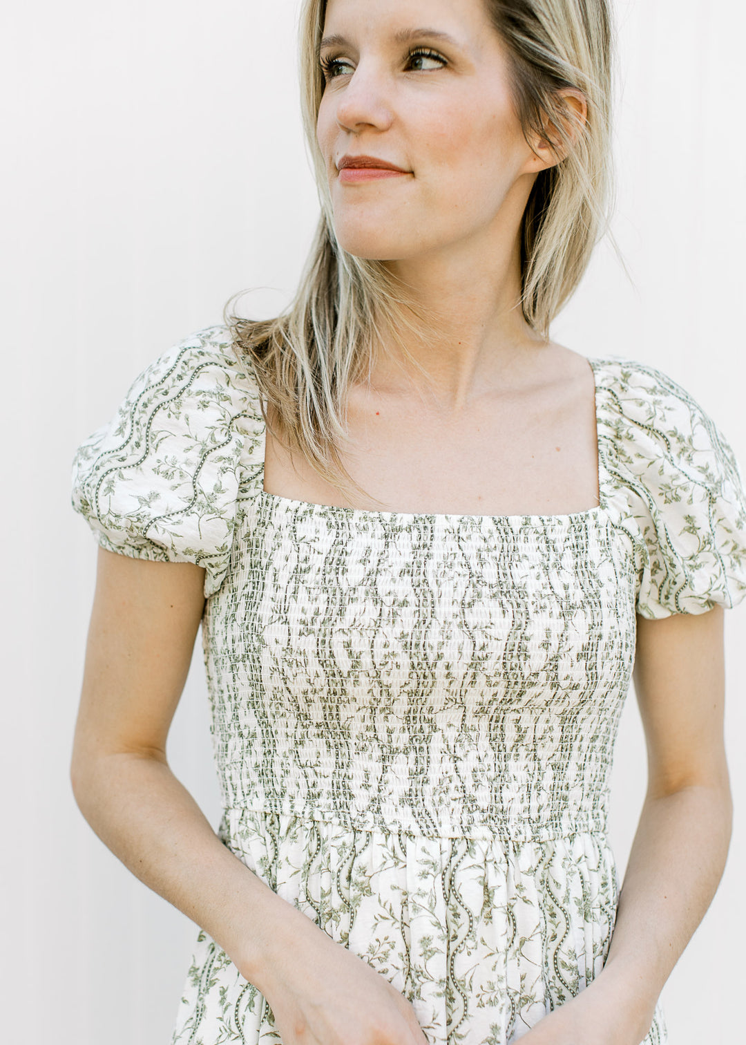Close up of square neck, short sleeves and smocked bodice on an off white midi with olive floral.