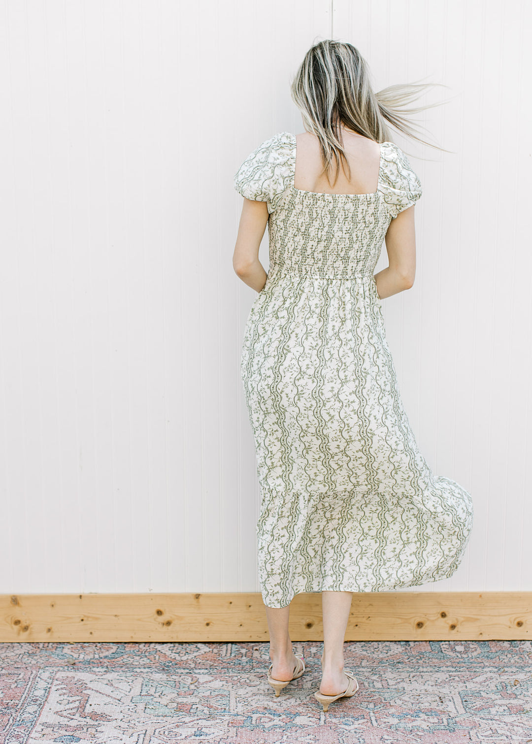 Back view of Model wearing an off-white midi with olive floral, square neck and smocked bodice.