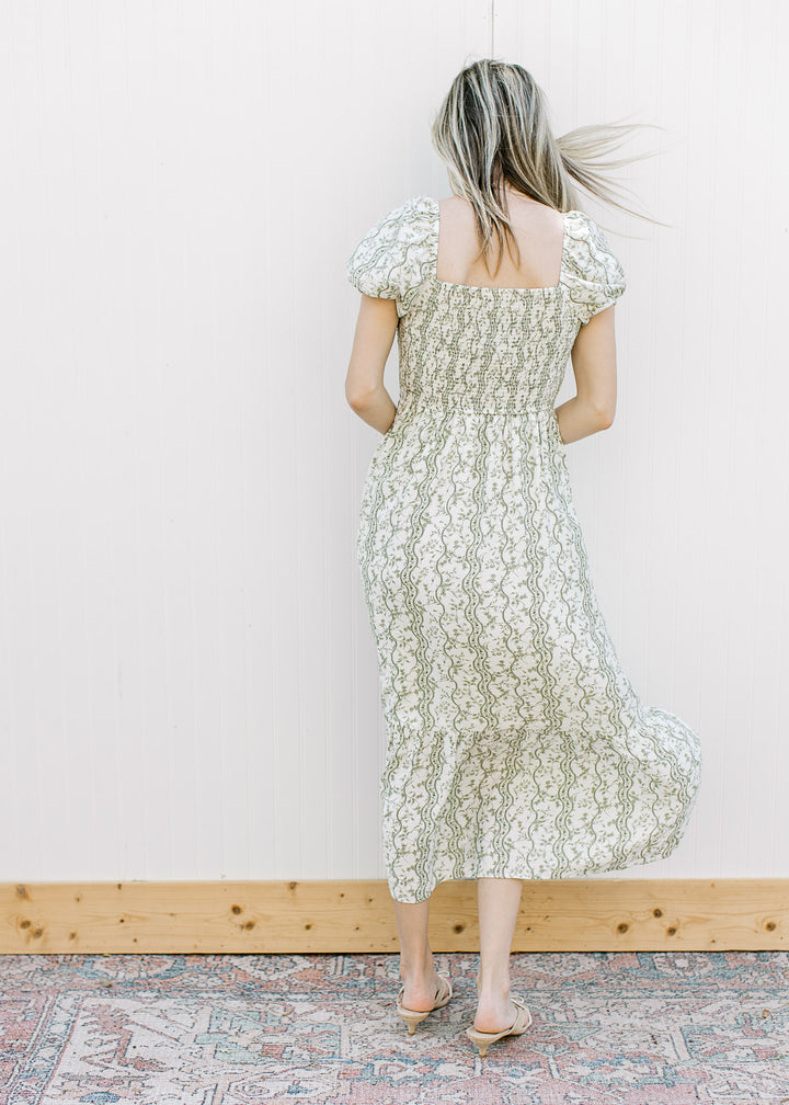 Back view of Model wearing an off-white midi with olive floral, square neck and smocked bodice.