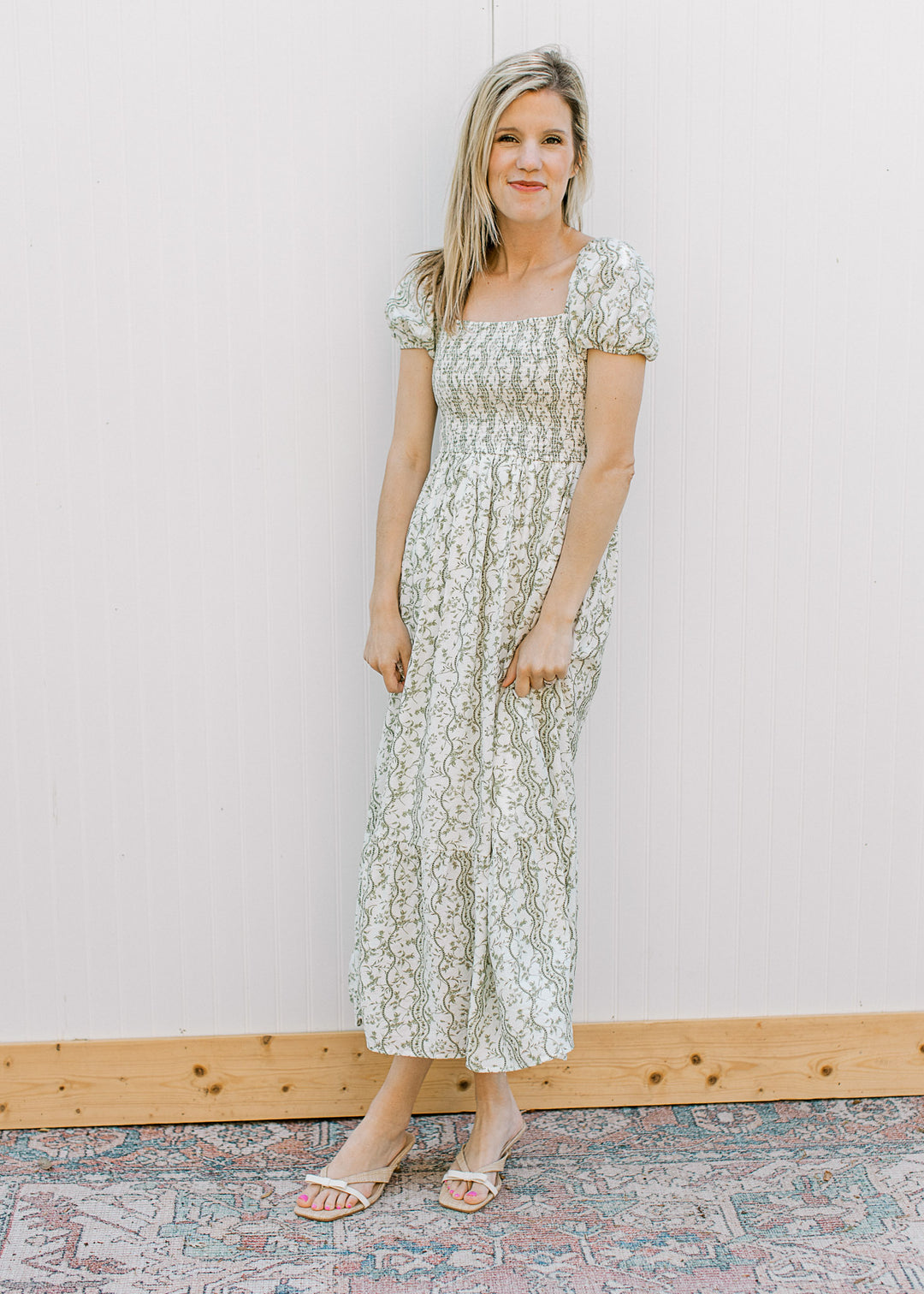 Model wearing heels and an off-white midi with olive floral, square neck and smocked bodice.
