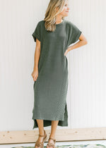 Model wearing a corded olive midi dress with hi-low design and cuffed short sleeves.