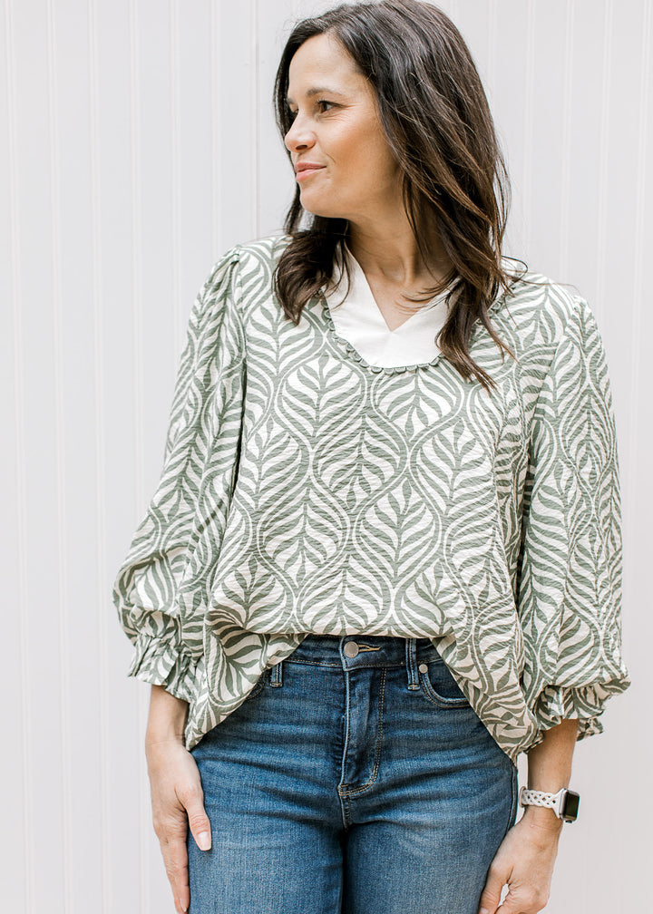 Model wearing a cream top with olive leaf pattern, cream v-neck yoke and 3/4 poet sleeves. 