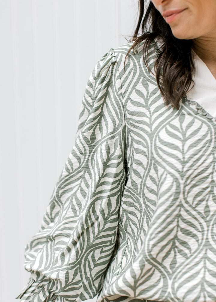 Close up of pleated shoulder on a 3/4 poet arm of a cream top with olive colored leaf pattern. 