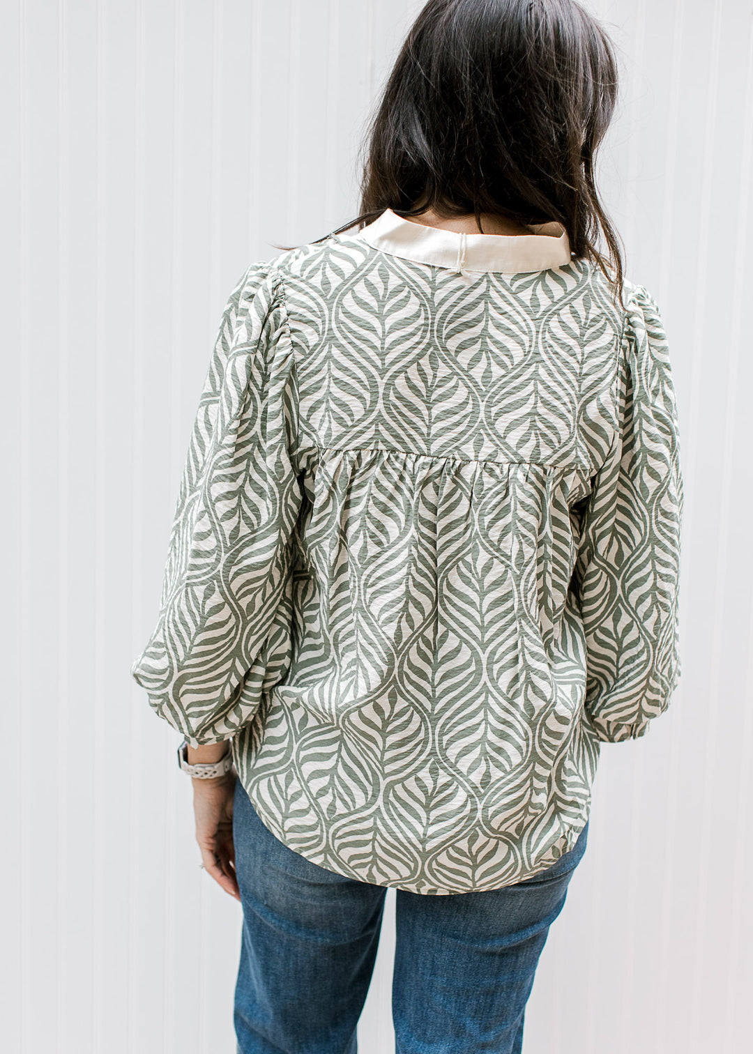 Back view of Model wearing a cream top with olive leaf pattern, cream yoke and 3/4 poet sleeves. 